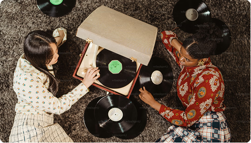 Two people sitting on the floor with vinyl records and a record player.